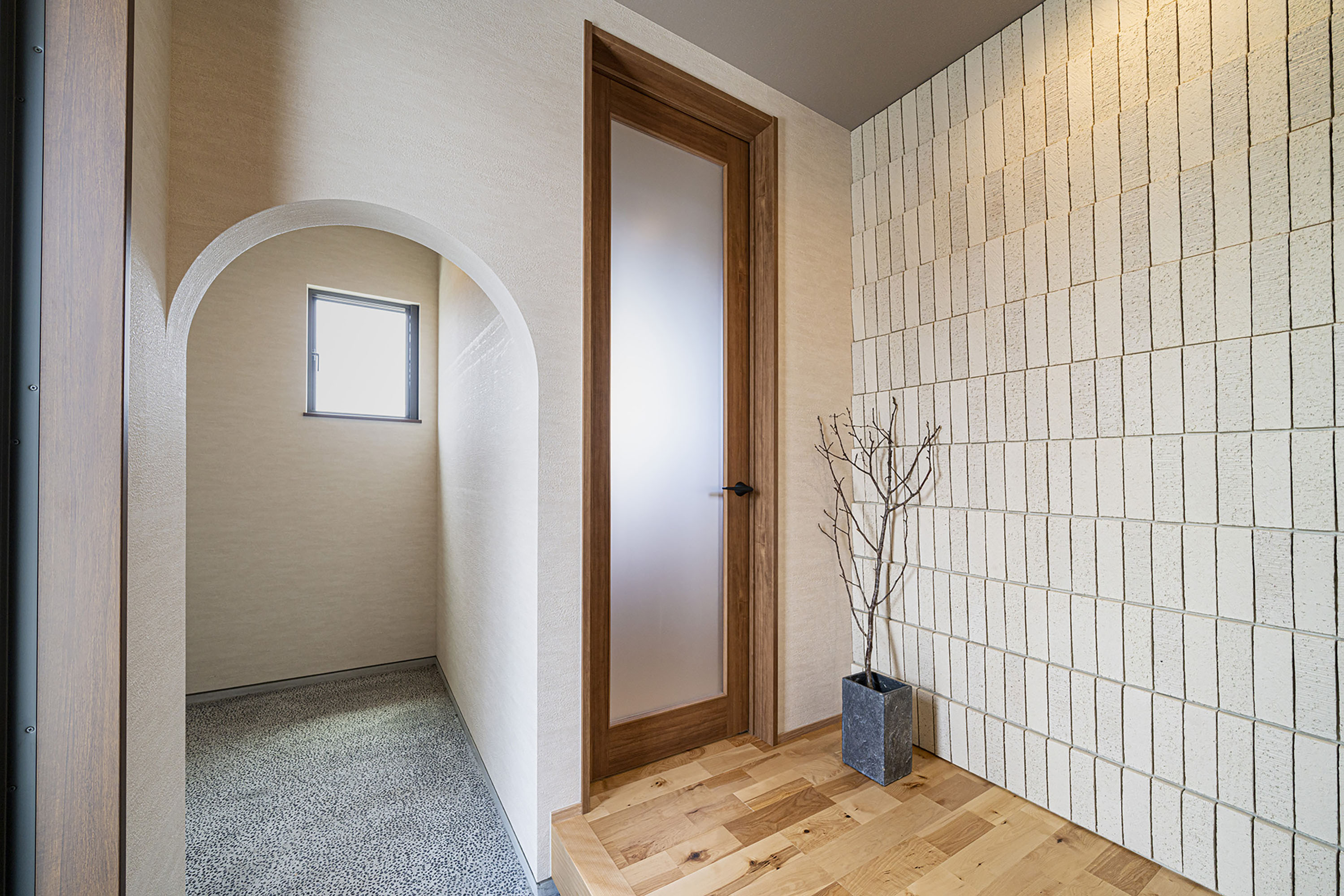 玄関には、アーチの垂れ壁が可愛い印象の土間収納を設計。洗い出しの土間、タイル壁、木の質感豊かなリビングドアなど、さりげない素材の良さが感じられる