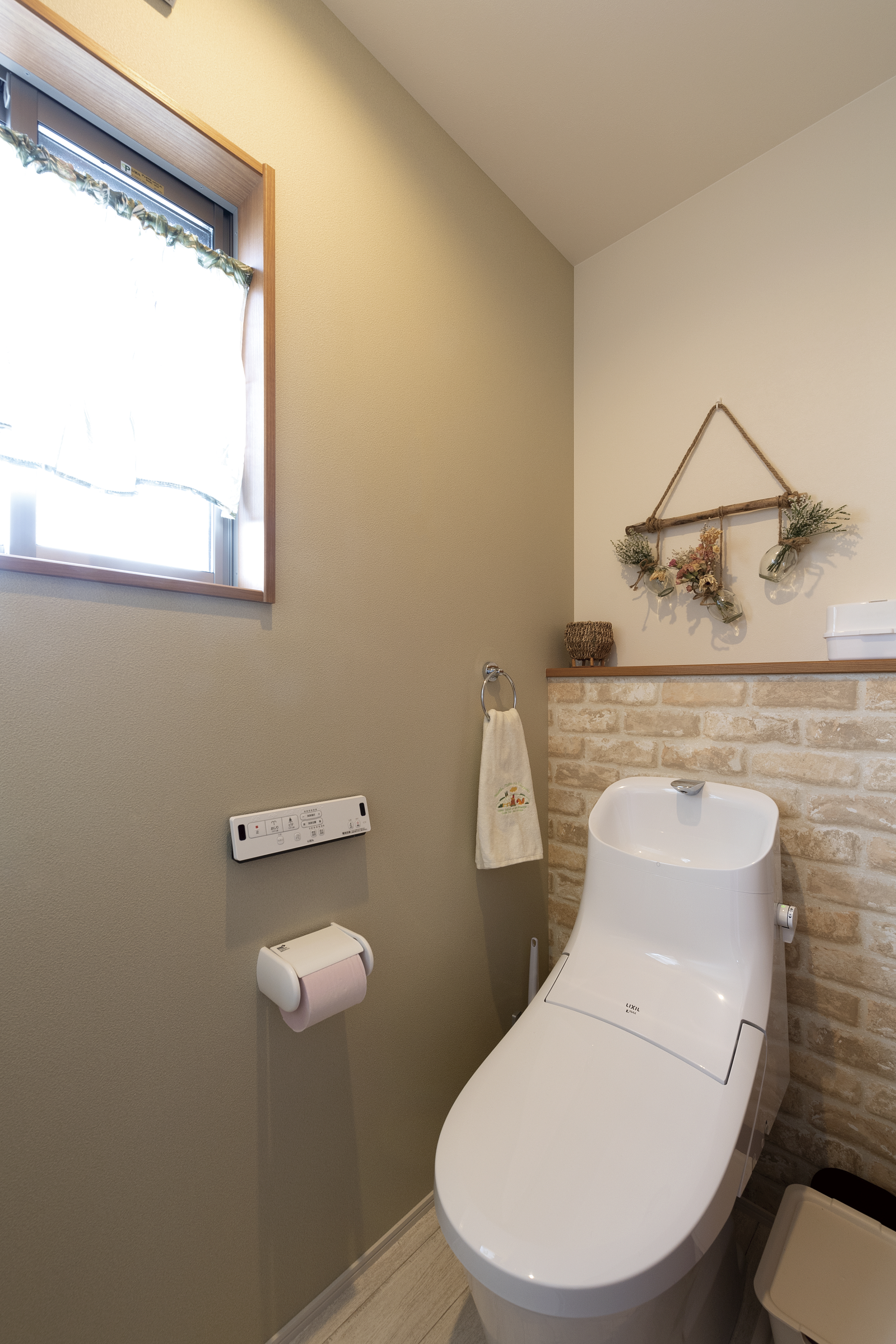 淡いグリーンやレンガ調の壁紙がナチュラルテイ ストの１階トイレ。妻のNさんが好きな可愛い雰 囲気に仕上げた